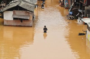 Personne traversant une rue inondée entre des habitations, situation nécessitant un plan de contingence face aux inondations.